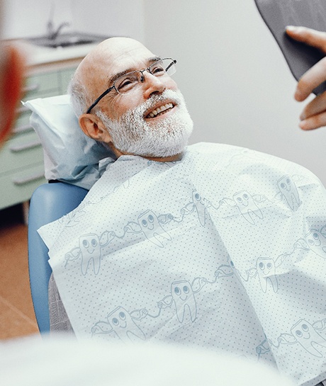 Man with glasses in dental chair smiling at reflection in mirror