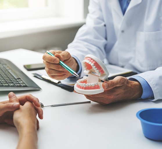 Hands of patient and dentist at desk with keyboard and model teeth